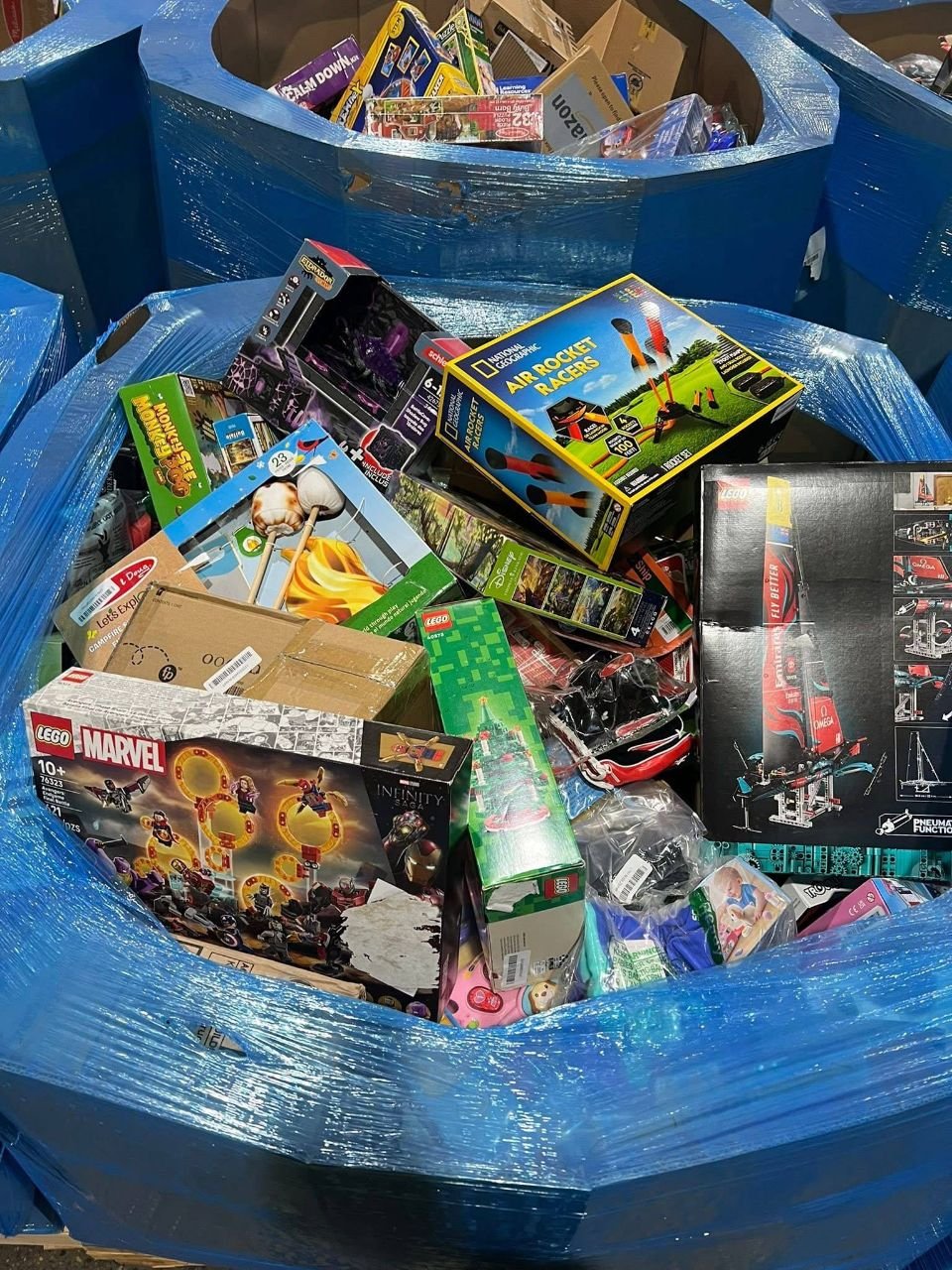 Brand-new mixed toy pallet with LEGO building sets and assorted boxed games in a blue bulk bin