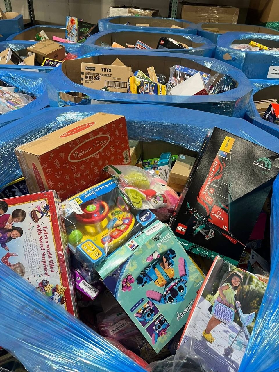 Multiple pallet bins of mixed toys games and branded boxed play sets in a warehouse