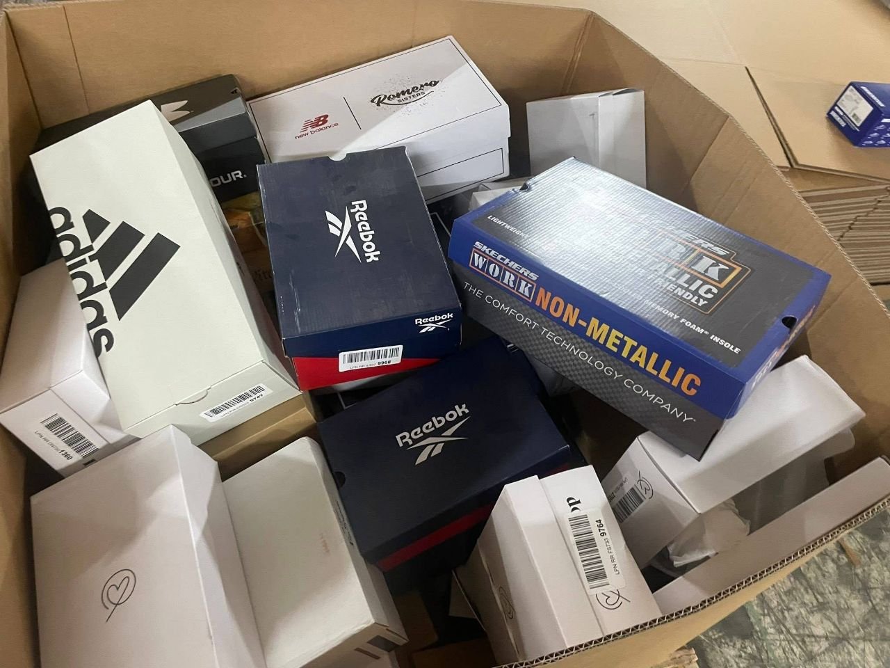 Box of assorted footwear inventory including Reebok Skechers and adidas shoe boxes
